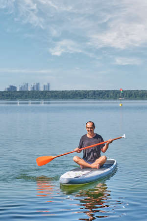 Asian older man on sup board on calm lake.の写真素材