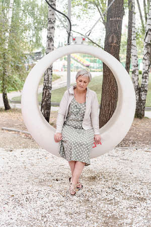 Sad caucasian senior woman sitting on round bench in park.の写真素材