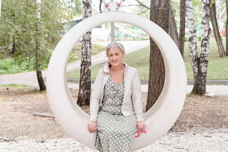 Sad caucasian senior woman sitting on round bench in park.の写真素材
