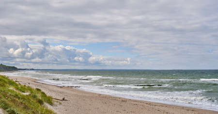 Beautiful seascape with waves, old wooden breakwater, sandy beach and cloudy sky.の写真素材