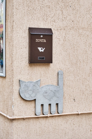 Mailbox and flat sculpture of smiling cat walking on pipe on wall with fish in its stomach.のeditorial素材