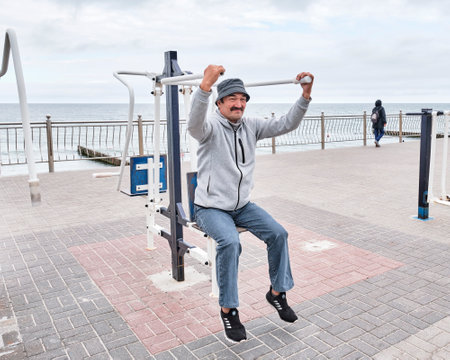 Senior Asian man in casual clothes works out on simulator in public area on waterfront.の写真素材