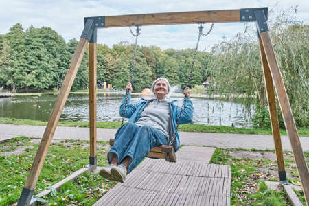 Happy senior caucasian woman with short gray hair swinging on chain swing in park