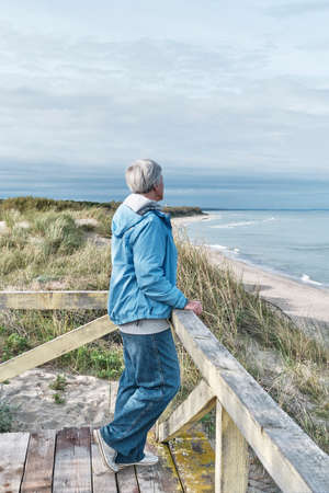 Senior woman with short gray hairon a wooden platform by the sea.. Travel conceptの写真素材