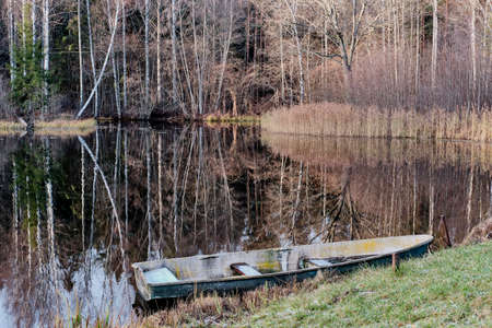 Autumn landscape. Old wooden boat moored to shore of calm lake surrounded by forest.の写真素材