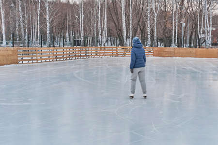 Senior woman in blue jacket and knitted hat skates on a skating rink in the park in winter.の写真素材