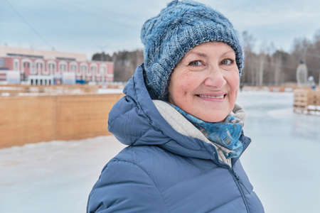 Close-up portrait of senior white woman, smiling and looking at camera, on a skating rink in winter.の写真素材