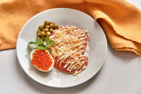 Salted red fish caviar on half of boiled chicken egg, slices of fresh red tomato under grated hard cheeseの写真素材
