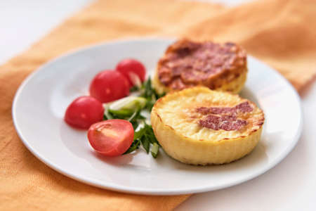 Two portioned round-shaped baked omelette, halves of cherry tomatoes, chopped green onions on white plate.の写真素材