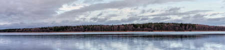 Beautiful landscape of late autumn on cloudy day. Mixed forest on shore of calm lake.Panorama.の写真素材