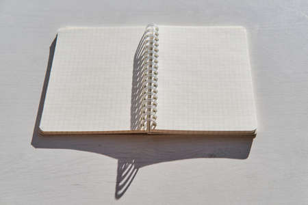An open blank notebook on a white table in bright sunlight, with hard shadows.の写真素材