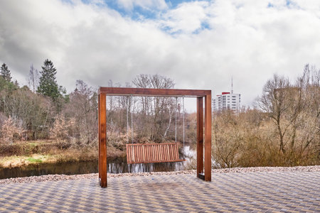 Modern wooden bench swinging on iron chains on embankment of Luga River, Russia.の写真素材