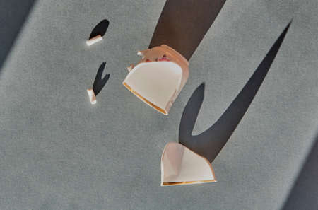 Shards of a broken white cup on a gray paper background with hard long shadows.の写真素材
