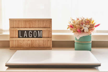 Beautiful bouquet of dried flowers and wooden sign with text LAGOM on white table next to laptopの写真素材