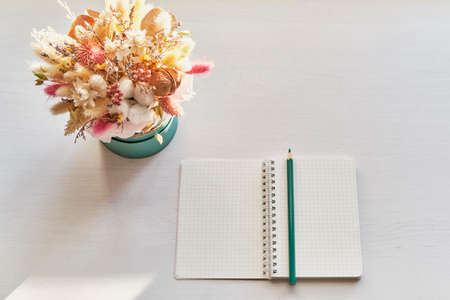 Beautiful fluffy bouquet of dried flowers, opened blank notebook with turquoise pencil on white table.の写真素材