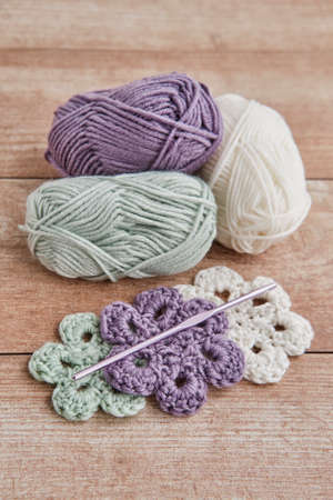Skeins of yarn, colorful knitted flowers and knitting hook on wooden table.の写真素材
