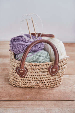 Skeins of yarn, wooden circular knitting needles in handmade straw basket on wooden tableの写真素材