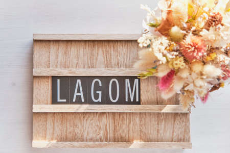 Wooden sign with text LAGOM on white table and defocused beautiful bouquet of dried flowers.Top viewの写真素材