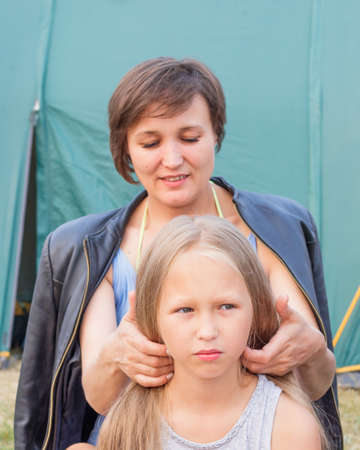 Mother styling long blond hair to her daughter in camping over of tent background.の写真素材