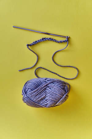 Crochet hook, chain of loops made of violet threads and skein of acrylic yarn on yellow background.の写真素材