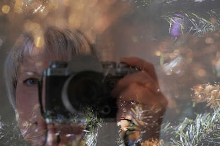 Mature woman takes self-portrait over of Christmas tree and blurred background. Christmas and New Year concept. Selective focusの写真素材
