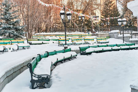 Snow-covered wooden benches in summer amphitheater of city park.の写真素材