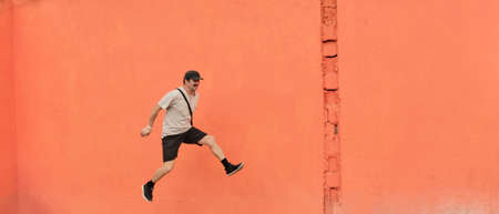Mature Asian man in casual clothes running through air over of bright orange wall background.の写真素材