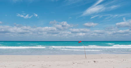 Red flag on sandy beach of Atlantic Ocean, Varadero, Cuba. Danger sign, no swimming.の写真素材