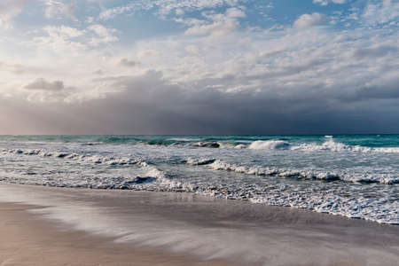 Dramatic scenic seascape. Waves, cloudy sky, sunlight. Sandy beach of Atlantic Oceanの写真素材