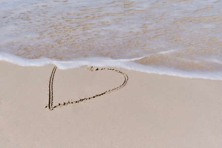 Wave coming to contour of heart drawn on white sand of tropical beach.
