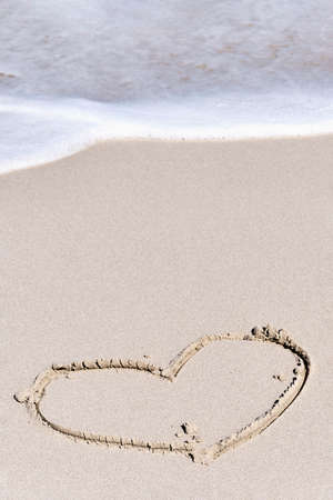 Form of heart drawing on white sand of tropical beach. Wave coming to drawingの写真素材