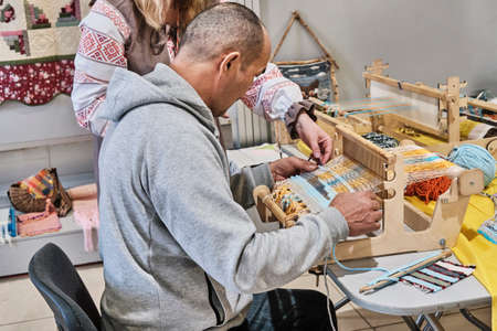 Faceless artisan woman teaching senior asian man to weaving small rug on table loom.の写真素材