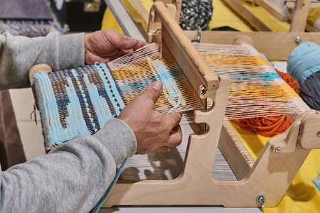 Hands of senior man weaving small rug with pattern on manual table loom.の写真素材