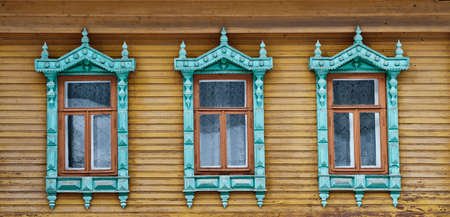 Three old windows with carved wooden architraves on shabby board wall.の写真素材