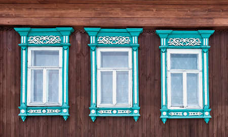 Three old windows with wooden turquoise architraves with patterns on brown board wall.の写真素材
