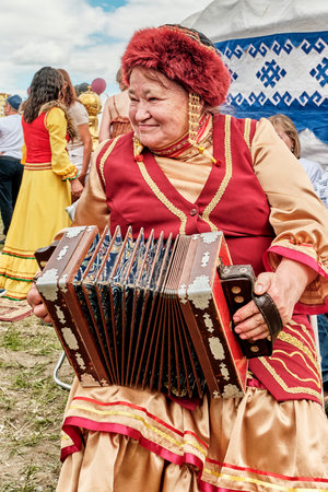 Senior woman in traditional Bashkir festive clothes playing national accordion at Sabantuy holidayのeditorial素材