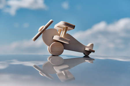 Wooden toy light aircraft biplane over background of cloudy sky on glossy surface.の写真素材