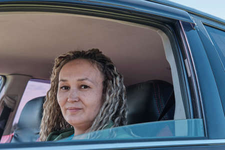 Close-up portrait of cute smiling middle aged asian woman in open car window.