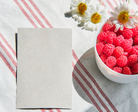 Greeting mockup scene on striped cotton napkin. Blank paper, cup with raspberries and daisy flowersの写真素材