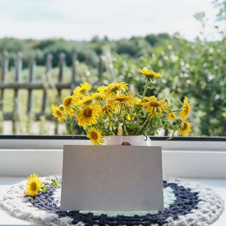 Greeting mockup scene on window sill of rural house. Blank paper, bouquet of wildflowersの写真素材