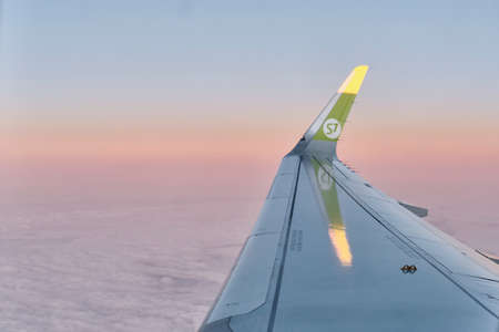 Wing of plane of Russian airline S7, flying in sky above clouds at dawn. Travel, transport concept