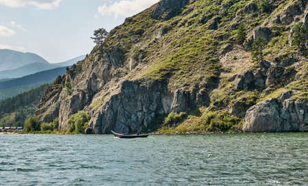 Man on fishing wooden longboat with motor moving to tent camp along cliff. Lake Baikal, Russia.の写真素材