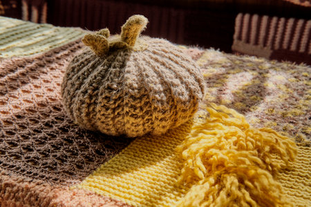 Knitted beige wool pumpkin on table covered with knitted patchwork tablecloth. Home decorationの写真素材