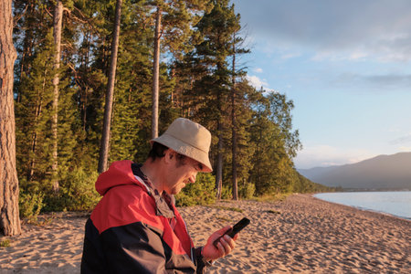 Senior asian man holding mobile phone on background of forest. Sandy beach of Lake Baikal, Russiaの写真素材