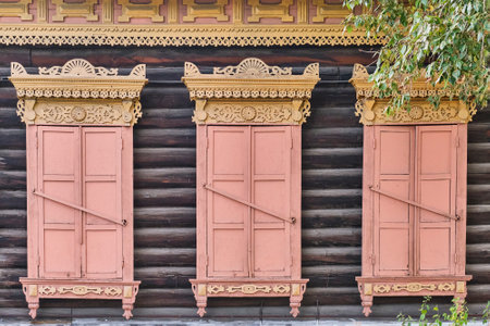 Old wooden painted windows. Carved yellow architraves, closed coral shutters. Ulan-Ude,Russia.の写真素材