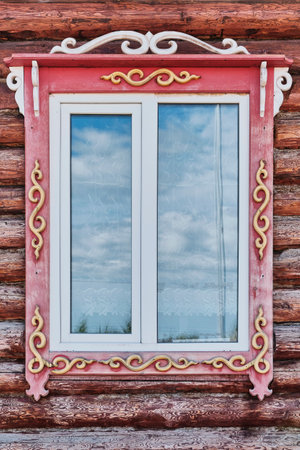 Window with carved wooden architraves and gold color pattern on log facade, Buryatia, Russia.の写真素材
