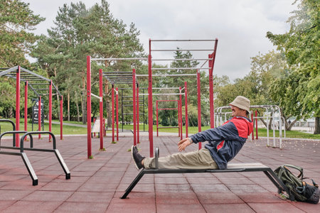 Senior Asian man in casual wear pumping up press on bench in sports equipped area of city park.の写真素材