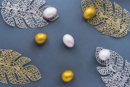 Gold and silver eggs, monstera leaves from wire on blue background.の写真素材