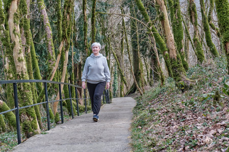 Senior active caucasian woman with gray hair cheerfully walking along a tourist trail in a relic forest. Full length front view. Yew-boxwood grove, Caucasian Nature Reserve, Russia.の写真素材