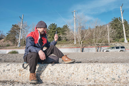 Senior Asian man, with mustache, wearing knitted hat and windbreaker, using mobile phone for video...